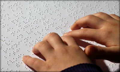 Immagine: foto di mani di bimbo che leggono un testo in Braille
